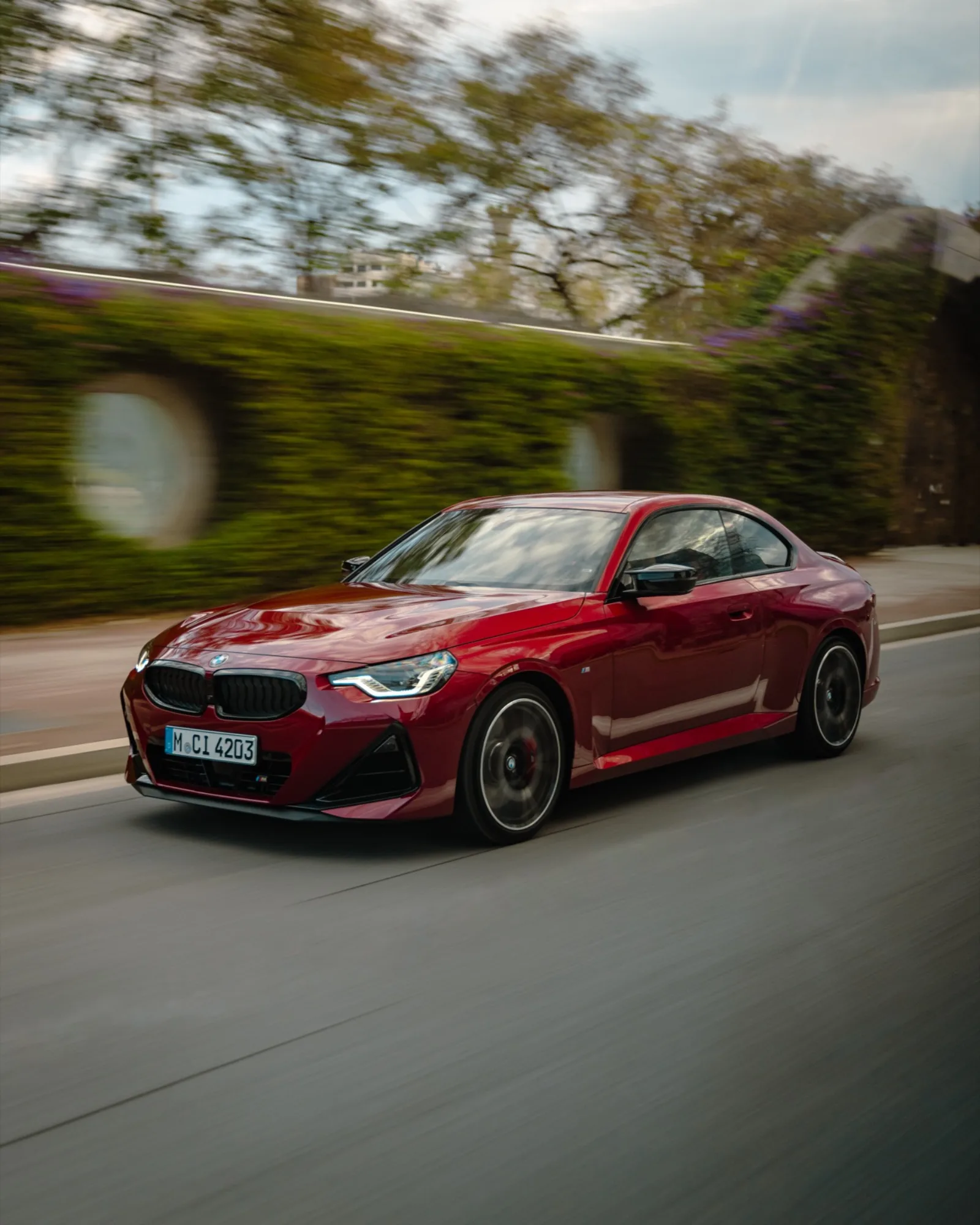 BMW 2 Serie Coupé in rood rijdend langs groene vegetatie